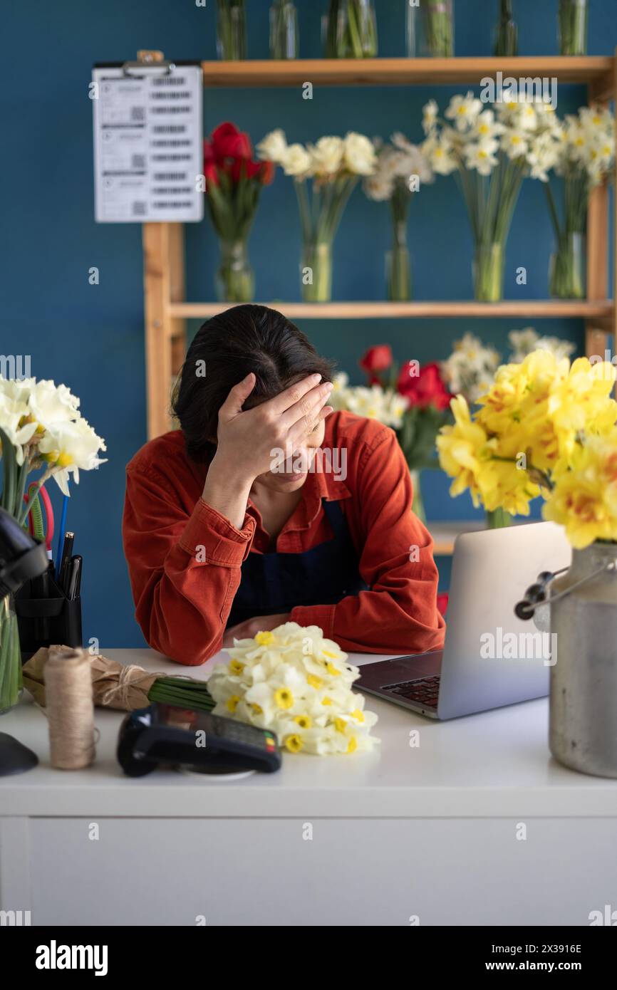 Floristin gestresst während der Arbeit am Laptop, müde Geschäftsfrau mit Kopfschmerzen in ihrem Blumenladen, fühlt sich krank bei der Arbeit Stockfoto