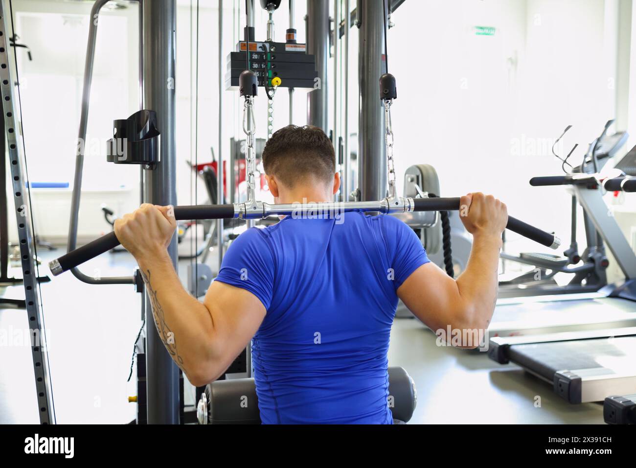 Junger schlanker Mann macht Übungen am Simulator in einem modernen Fitnessstudio, Rückansicht Stockfoto