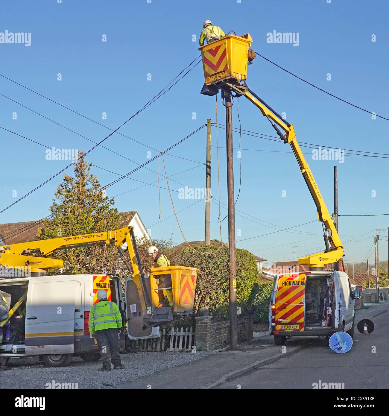 Elektroingenieure, die in Wohngebäuden arbeiten, die am Wintertag des blauen Himmels in England Großbritannien die Oberleitungen ersetzen Stockfoto