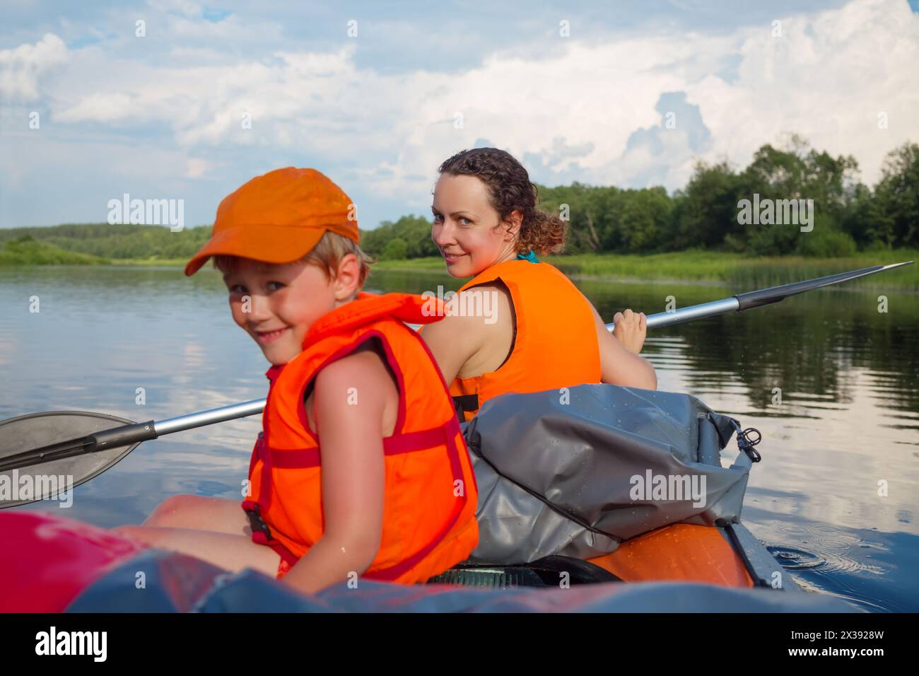 Kleiner Junge und Frau in Schwimmwesten segeln im Sommer auf einem Schlauchboot auf dem Fluss, konzentrieren Sie sich auf die Frau Stockfoto