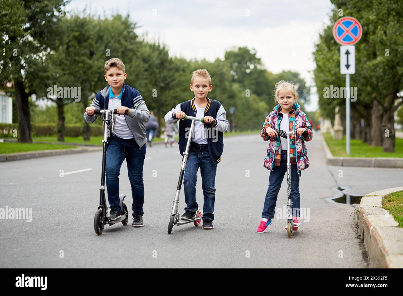 Zwei Jungs und Mädchen stehen mit Schubrollern auf der Straße. Stockfoto