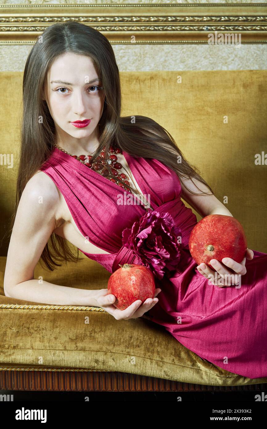 Die junge Frau lehnt sich auf der Couch und hält Granatäpfel in der Hand. Stockfoto