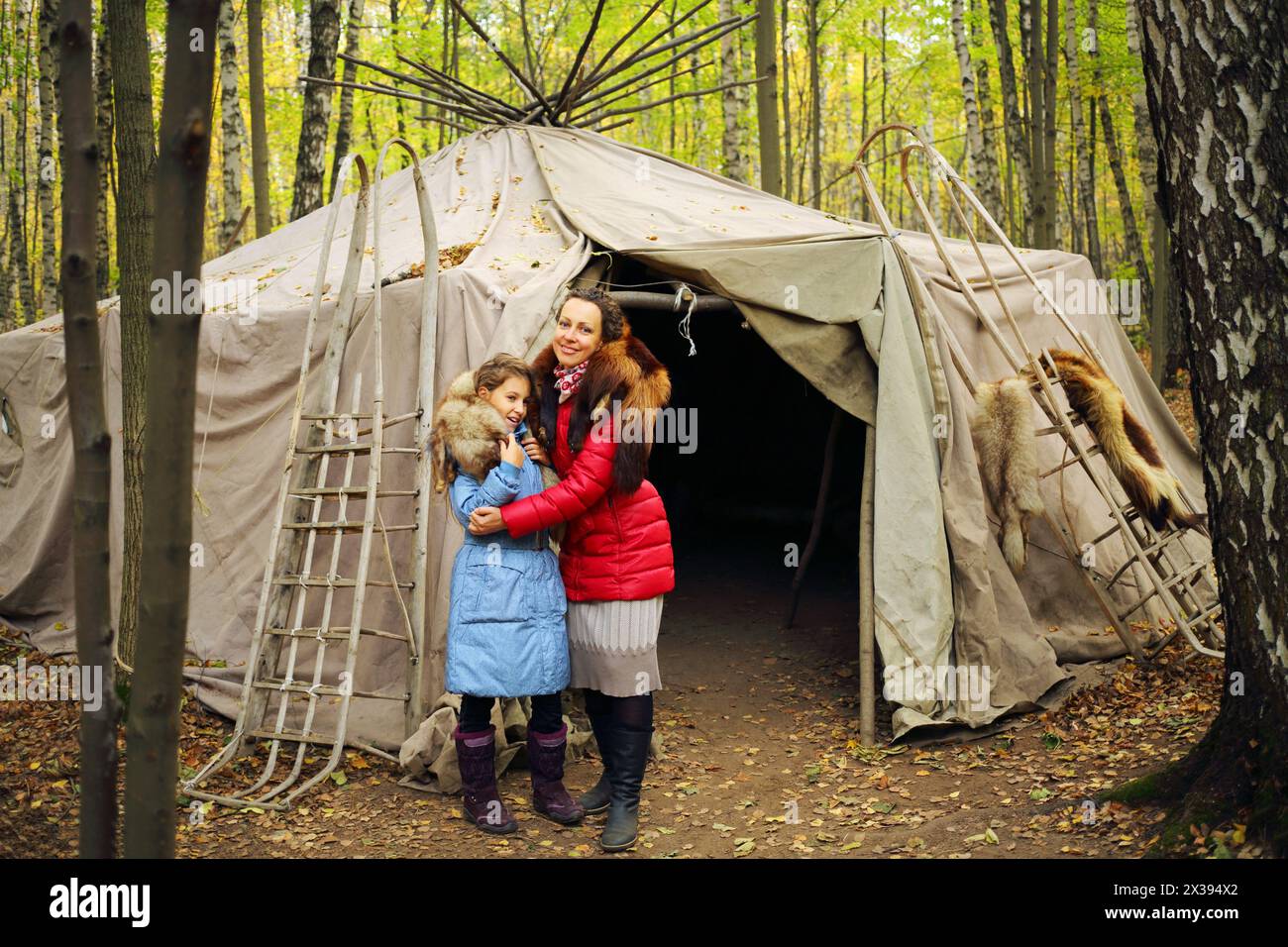 Frau und Tochter stehen in der Nähe der Chukot-Jurte mit Schlitten im Herbstwald Stockfoto