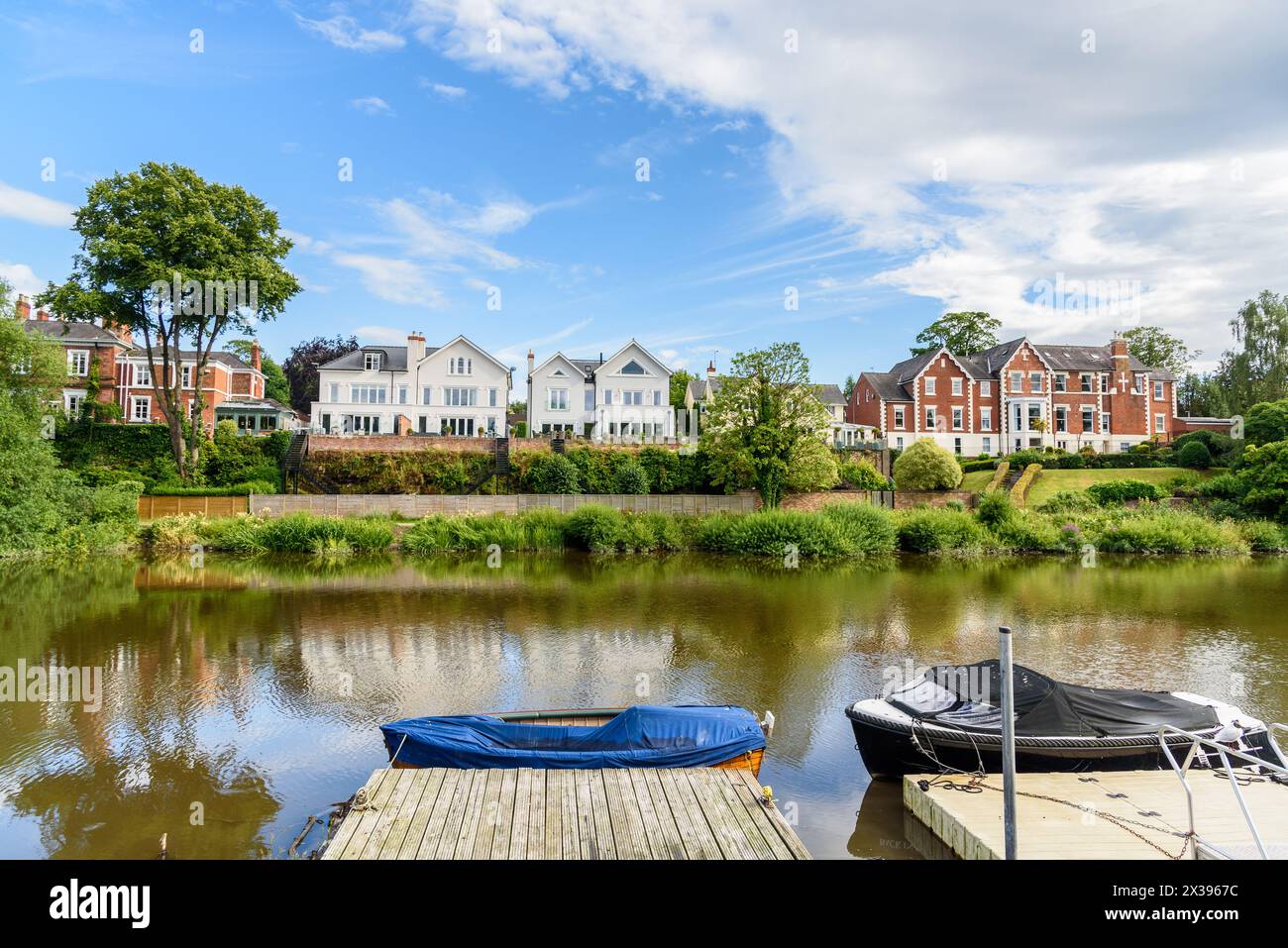 Häuser am Flussufer an einem sonnigen Sommertag. Zwei Boote, die an den Anlegestellen liegen, sind im Vordergrund. Stockfoto