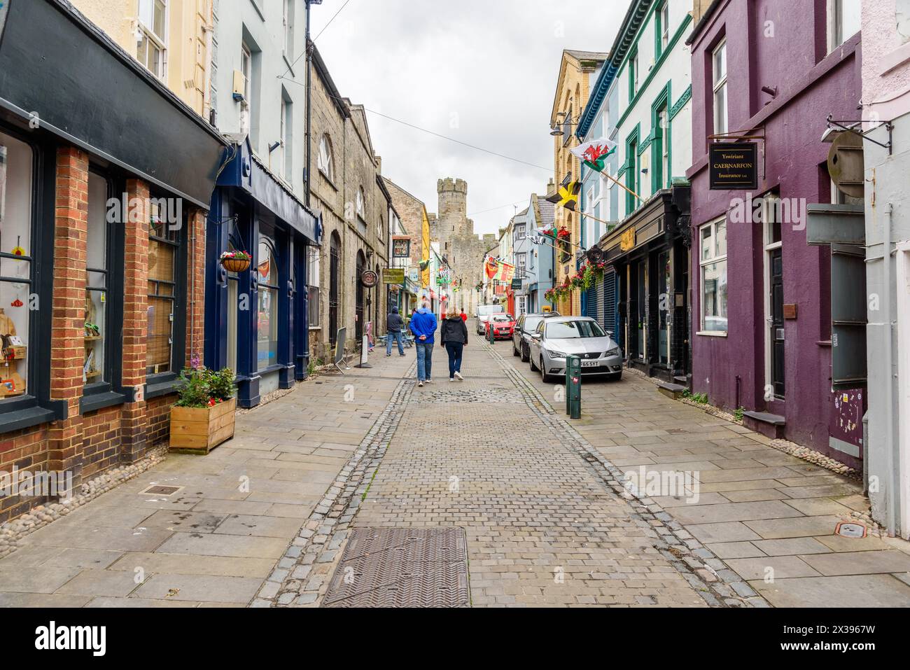 Caernarfon, Wales, Vereinigtes Königreich - 10. Juli 2023: Menschen gehen entlang einer engen Kopfsteinpflasterstraße in der ummauerten Altstadt Stockfoto