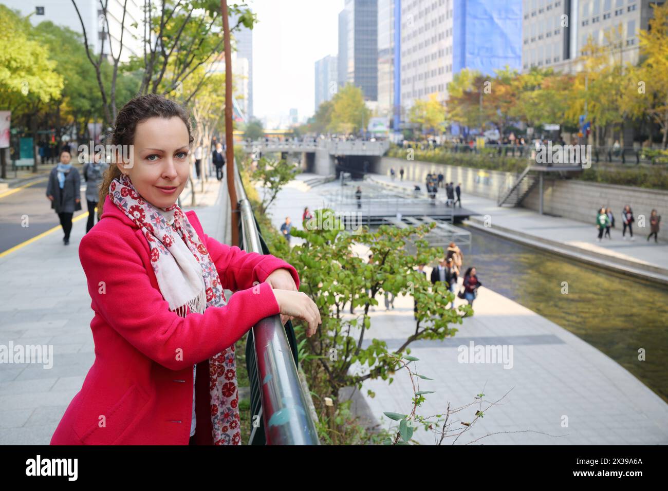 Frau in rotem Mantel, die neben der Barriere steht und den Hangang River in Seoul beobachtet Stockfoto