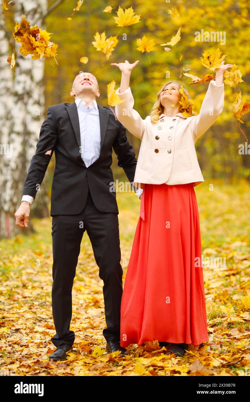 Schöne Frau und Mann werfen Blätter im gelben Herbstpark Stockfoto