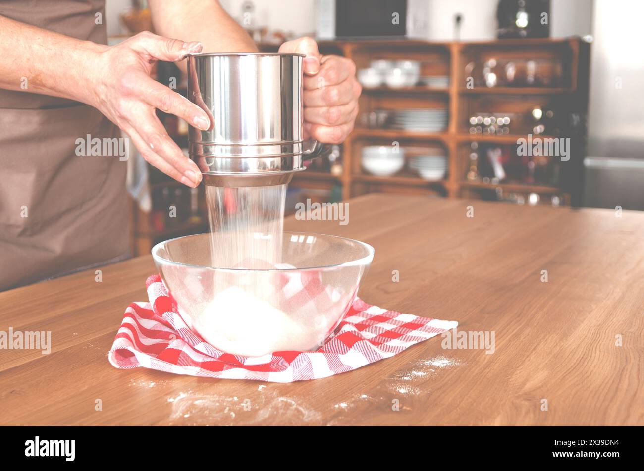 Mehl in einer Schüssel auf einem Holztisch in einer mit Schränken gefüllten Küche sieben Stockfoto