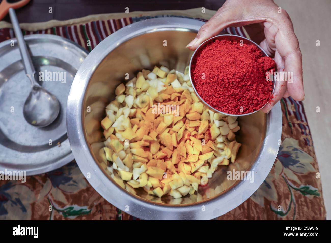 Hausgemachte rohe Mangobeizungsmittelherstellung mit Mango, rotem Chillpulver, Kurkuma und anderen Masalas in der indischen Küche mit Utensilien aus Edelstahl. Stockfoto