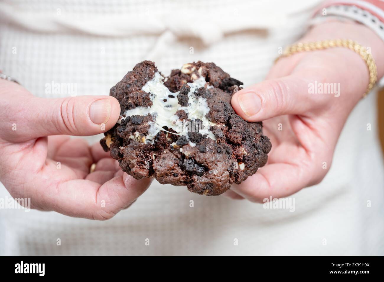 Ein frisch zubereiteter, warmer Oreo-Cookie im NY-Stil, der vom Bäcker auseinandergezogen wird. Der Keks ist mit einer weißen Schokoladencreme gefüllt Stockfoto