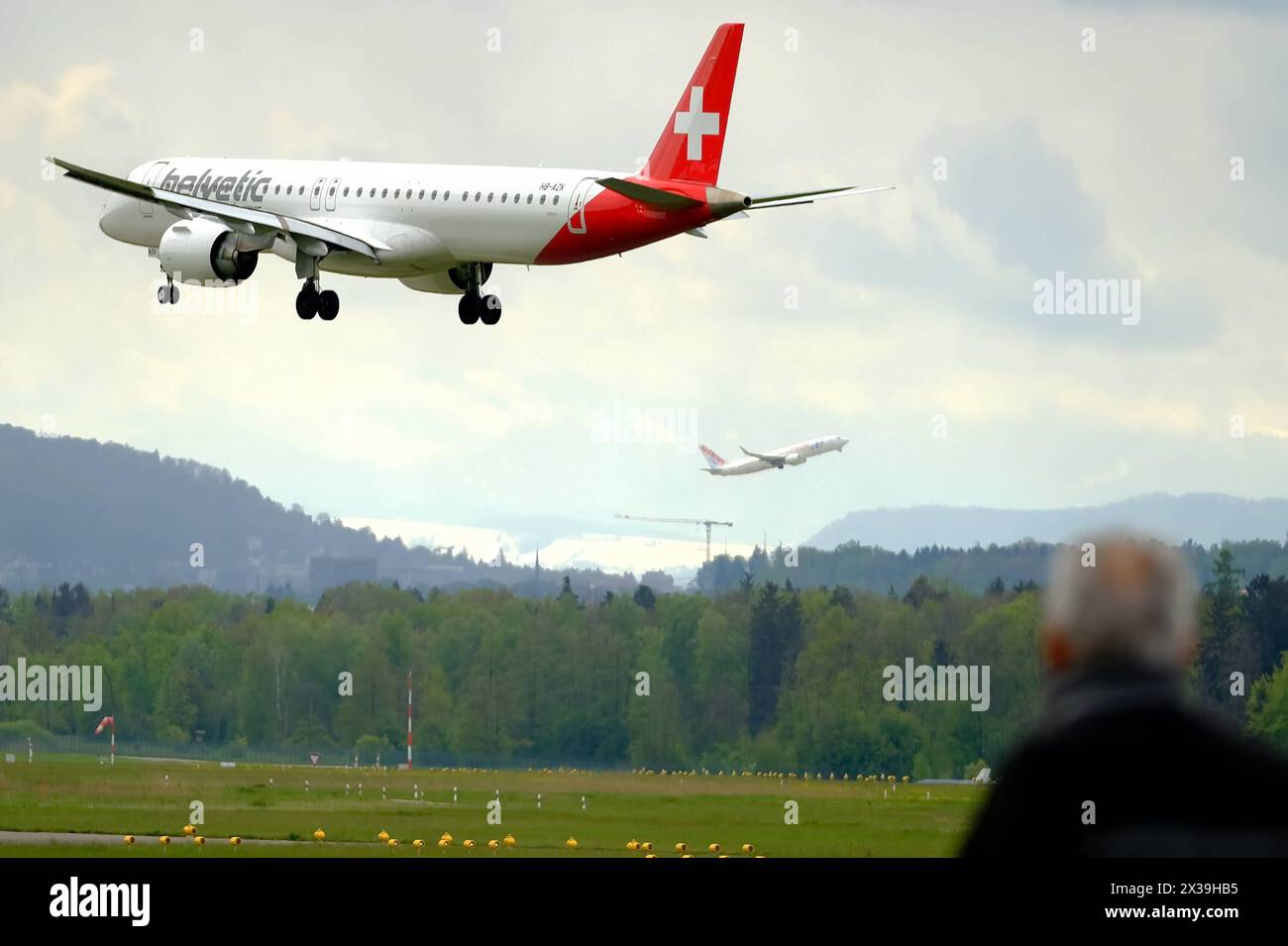 REKORDDATUM NICHT ANGEGEBEN Helvetic Airlines Embraer E195-E2 ERJ 190-400 STD mit Registrierung HB-AZK landet auf dem Flughafen Kloten, Zürich, während ein Spotter sie und ein anderes Flugzeug von einer anderen Start- und Landebahn abheben beobachtet Copyright: XSergioxBrunettix Stockfoto