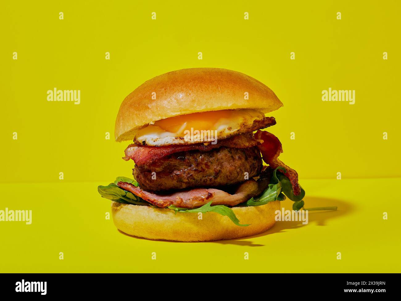 Hamburger mit Speck und Ei in einem Brötchen auf gelbem Hintergrund. Stockfoto