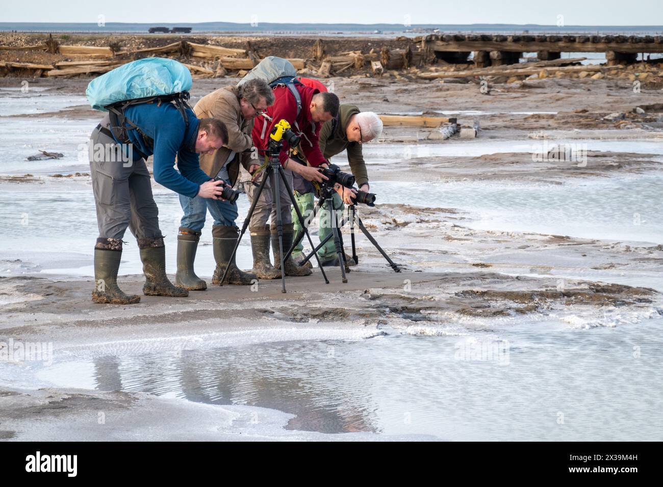 Baskuntschak, Russland - 18. April 2024: Eine Gruppe von Fotografen, die mit Rucksäcken und Stativen ausgestattet sind, bewegt sich am gefrorenen Seeufer und konzentriert sich dabei auf das schroffe, vereiste Gelände. Stockfoto