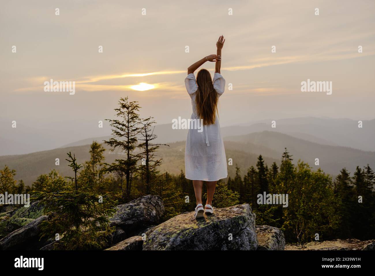 Eine Frau, die triumphierend auf dem Gipfel eines Berges steht und ihre Arme hochhält, um ihre Leistung und die atemberaubende Aussicht zu feiern. Stockfoto