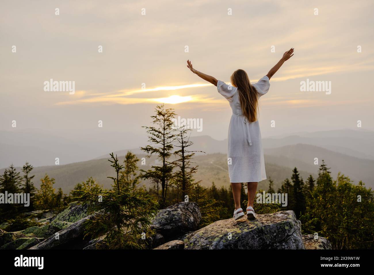 Eine Frau steht triumphierend auf einem Berg mit ausgestreckten Armen und zeigt ein Gefühl von Erfolg und Sieg gegen den Berg b Stockfoto