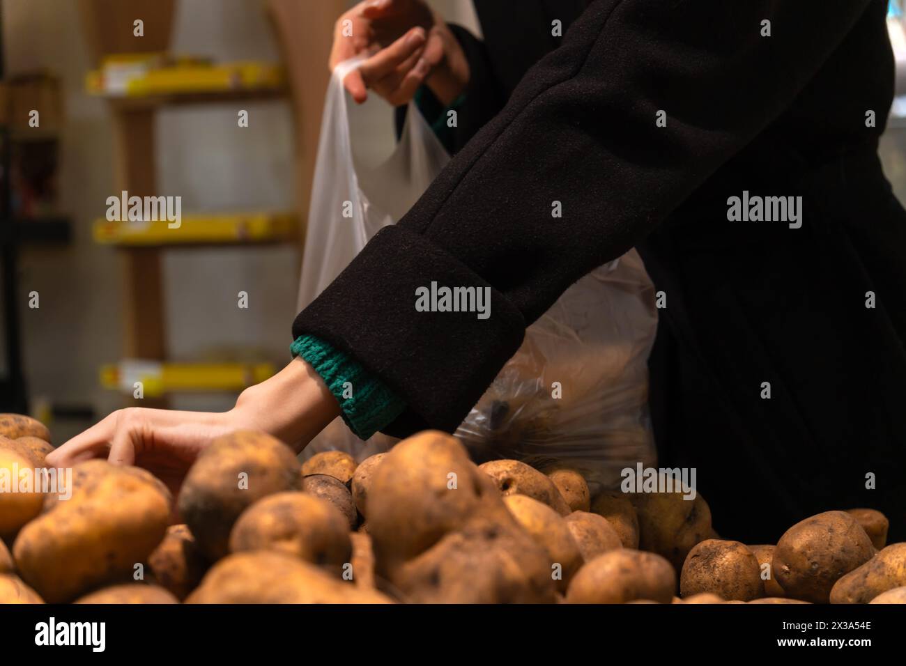 Eine Frau in einem schwarzen Mantel packt Kartoffeln in einem Supermarkt. Kartoffeln im Laden kaufen. Stockfoto