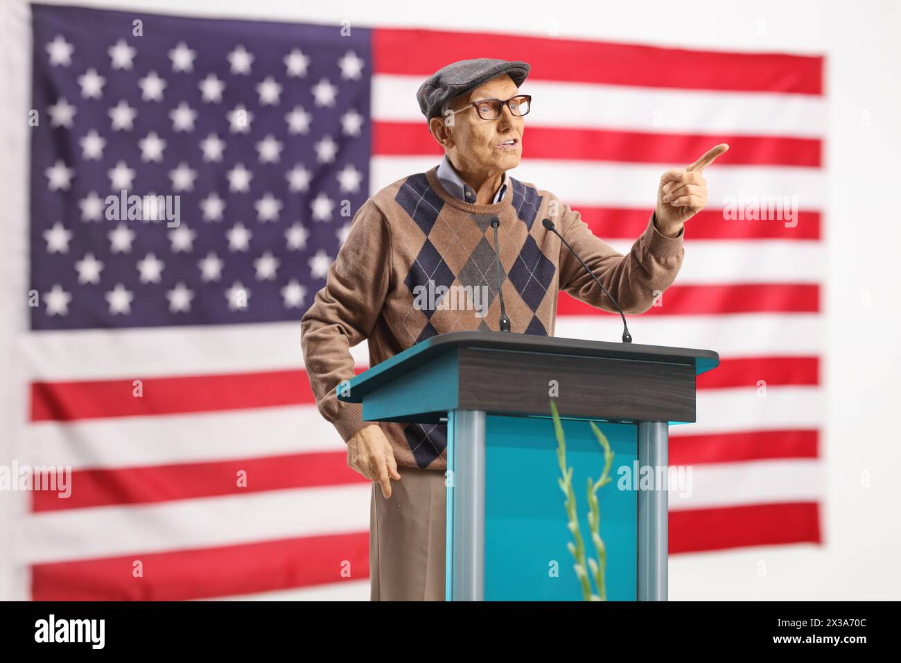 USA-Flagge und reifer männlicher Lautsprecher, der auf einem Sockel spricht und mit dem Finger Gesten macht Stockfoto