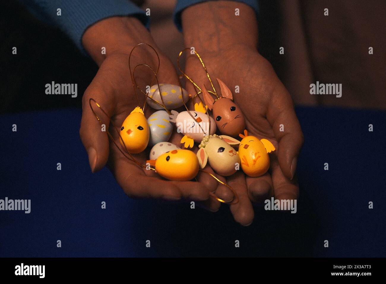 Frau, die Osterspielzeug-Anhänger in der Hand hält. Gelbe, lustige kleine Küken, Hasen, Kaninchen. Niedliche Festdekoration. Dunkle Frühlings-Feiertags-Tapete. Stockfoto