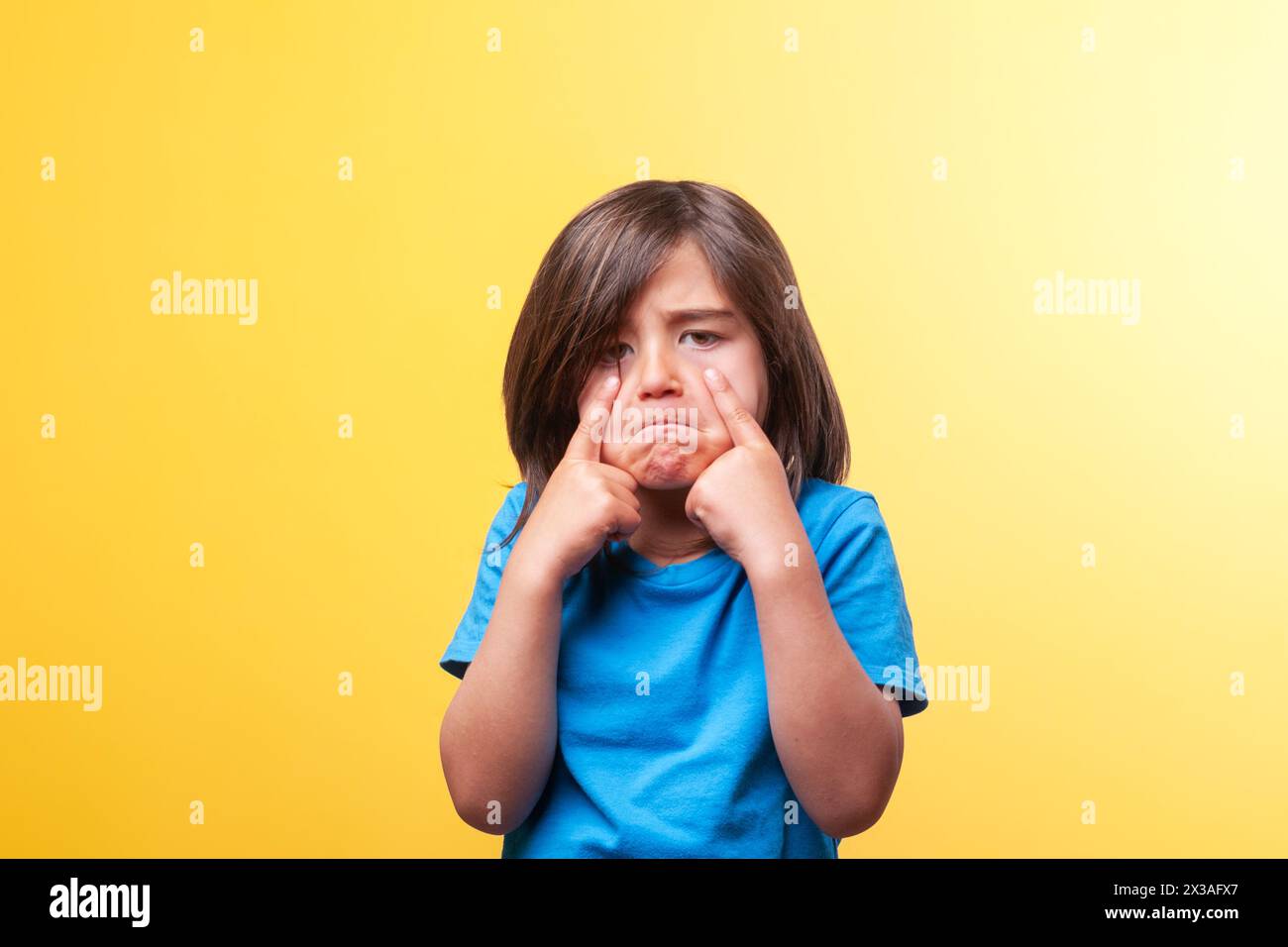 Ein Junge mit langen braunen Haaren, einem traurigen Gesicht und den Fingern seiner Hand zeigt, dass er weint. Das Konzept von Traurigkeit, Weinen, Trauer und Trauer. Stockfoto