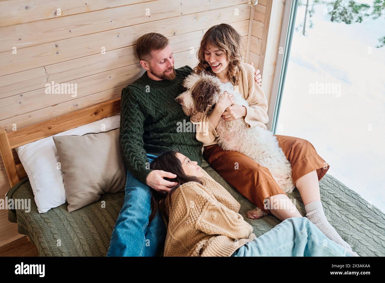 Blick aus dem Hochwinkel, moderne Familie mit Hund, die den Wintertag zu Hause verbringen und sich im Schlafzimmer in einem Holzhaus entspannen Stockfoto