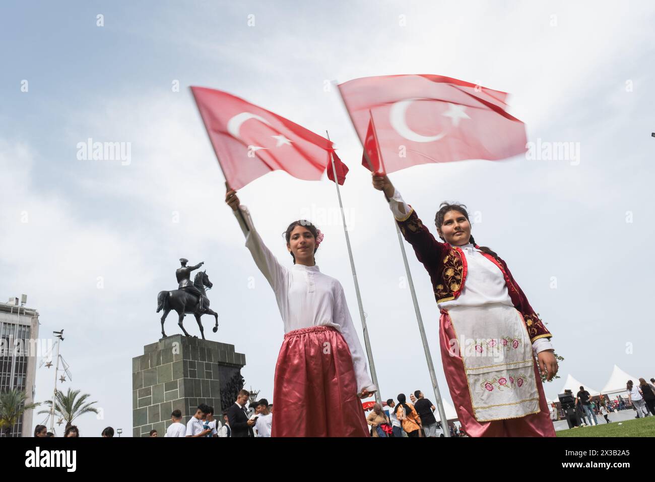 Izmir, Türkei - 23. April 2024: Zwei fröhliche Mädchen schwenken während der Feierlichkeiten zum Kindertag mit traditionellen Demonstrationskleidern die türkische Flagge. Stockfoto