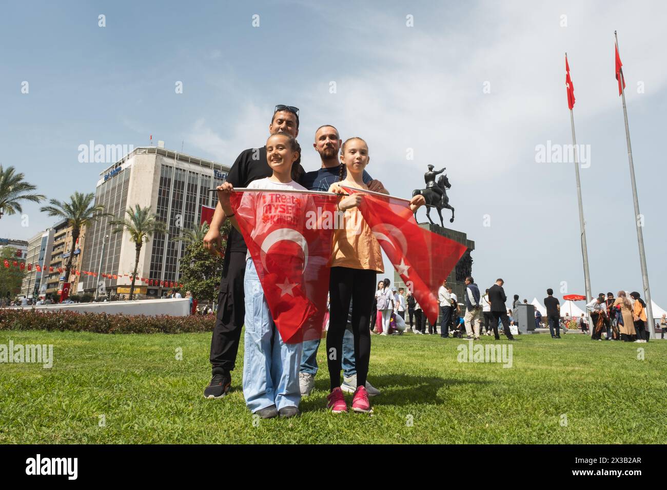 Izmir, Türkei - 23. April 2024: Während der Feierlichkeiten zum Kindertag auf dem Platz der Republik stehen zwei Mädchen mit Fahnen stolz mit ihrem Vater, mit dem Stockfoto