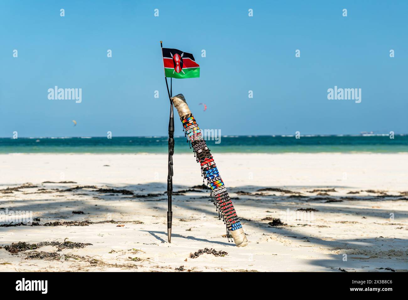 Der Speer von Masai und die Nationalflagge von Kenia vor dem Hintergrund einer wunderschönen Strandlandschaft. Das Konzept des afrikanischen Tourismus. Stockfoto