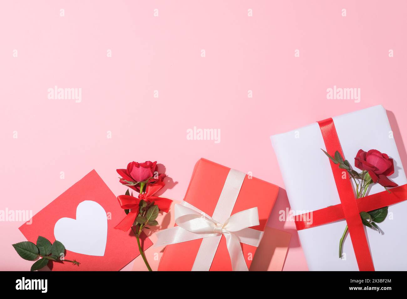 Der Hintergrund in Pastellrosa war mit einigen Geschenkboxen und einer handgefertigten Geschenkkarte mit roten Rosen dekoriert. Leeres Feld für die Produktpräsentation. Inhalt von Int Stockfoto