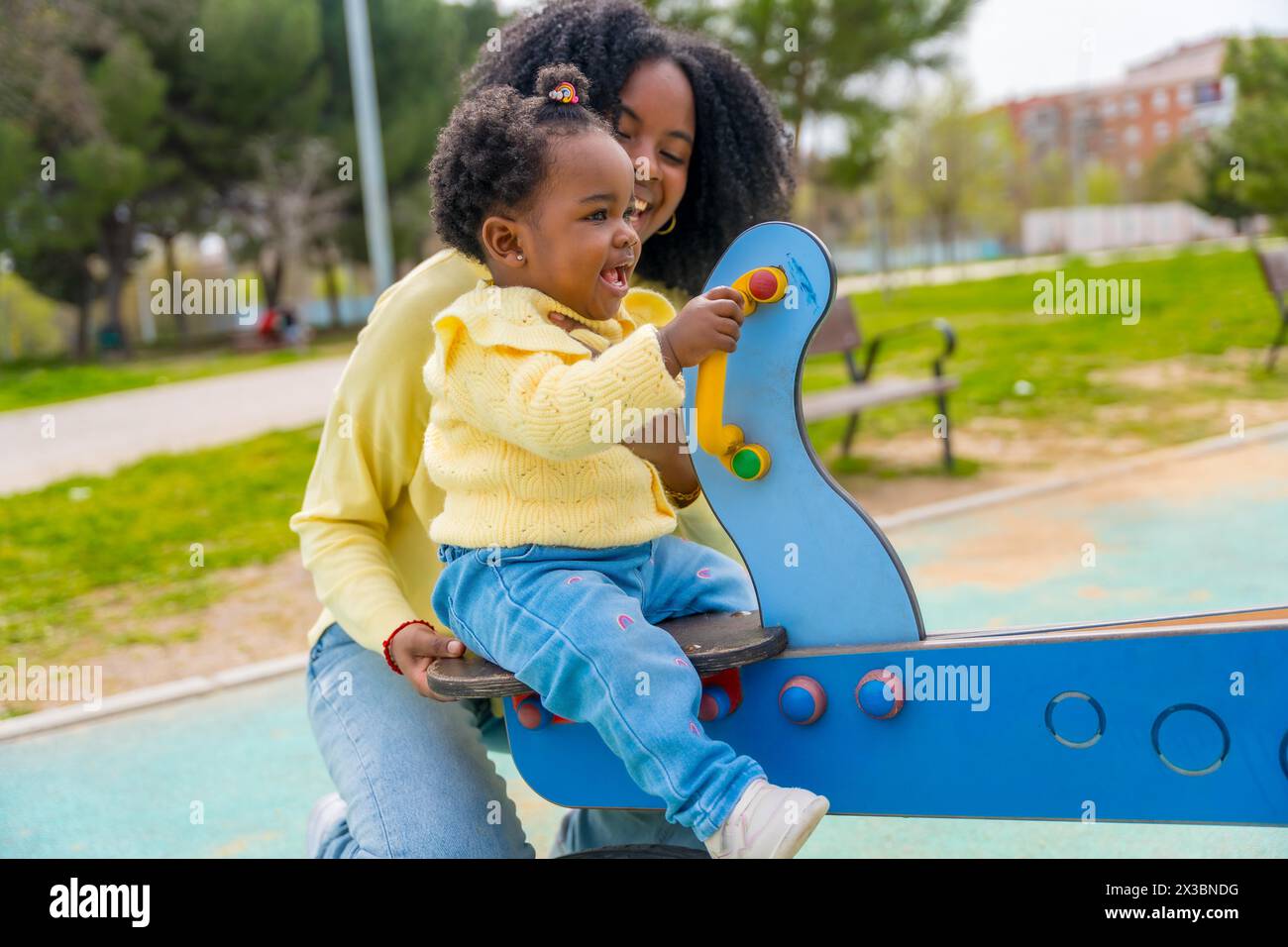 Afrikanische Tochter, die mit ihrer Mutter in einem öffentlichen Park eine Schaukel genießt Stockfoto