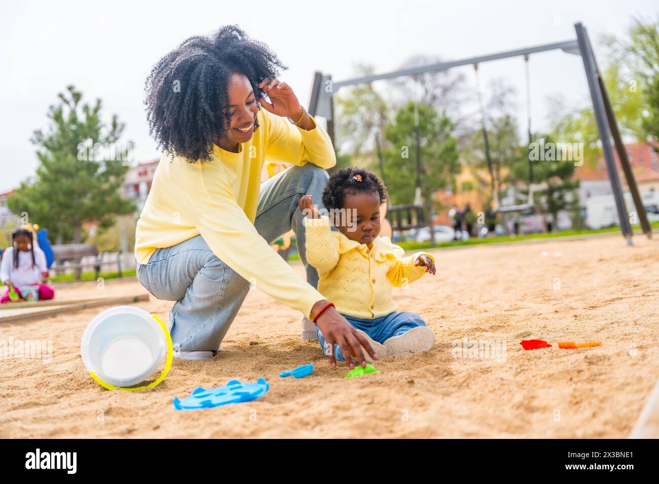 Glückliche afrikanische Mutter und Tochter sitzen auf dem Sand des Parks und spielen zusammen Stockfoto