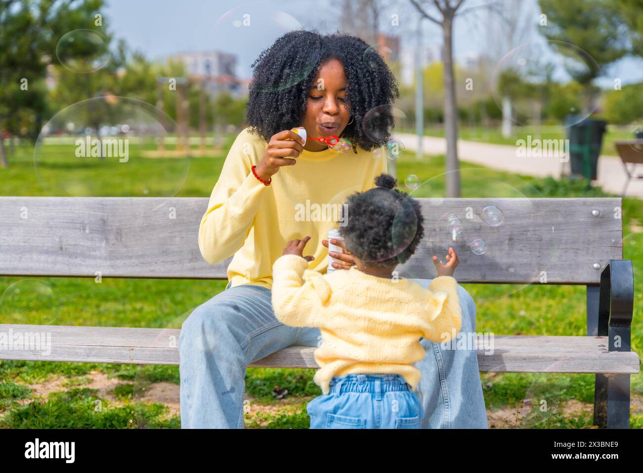 Frontales Dreiviertelfoto einer afrikanerin und Tochter, die in einem Park mit Seifenblasen spielen Stockfoto