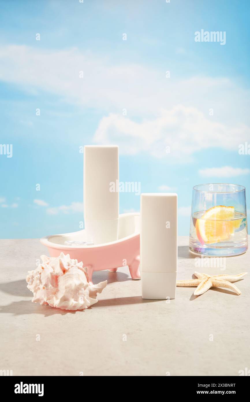 Zwei weiße Flaschen mit leerem Etikett, verziert mit Seesternen, Muschelschale und einem Becher mit Wasser und einer Orangenscheibe. Das Konzept des Sommerrekreats Stockfoto