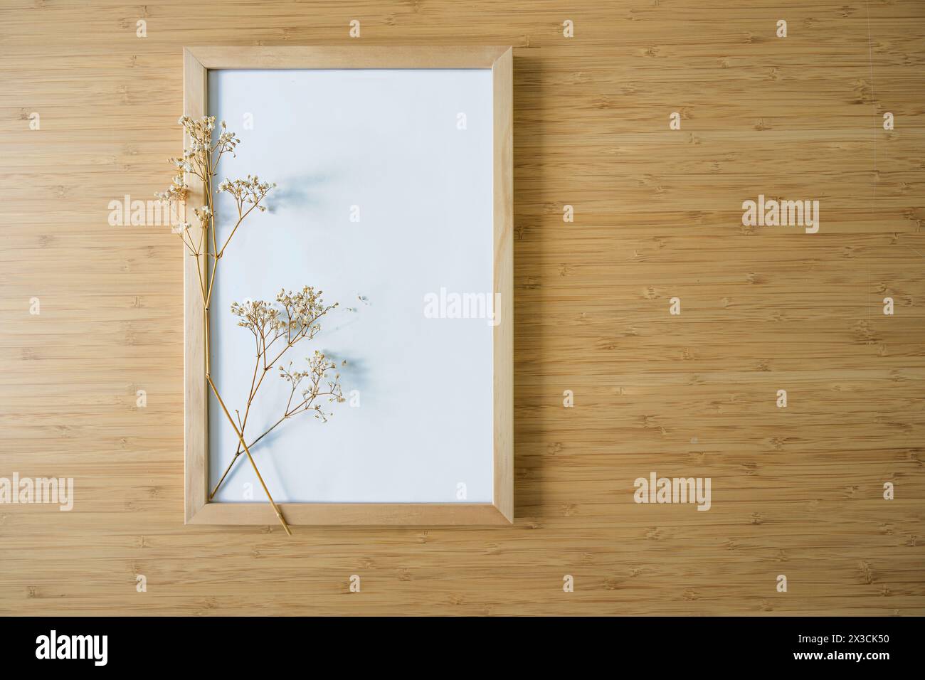 Kleiner gypsophila-Zweig auf einem leeren Bilderrahmen auf Bambushintergrund, Stillleben und Wohnkultur im minimalistischen Japandi-Stil, Hintergrund für Produ Stockfoto