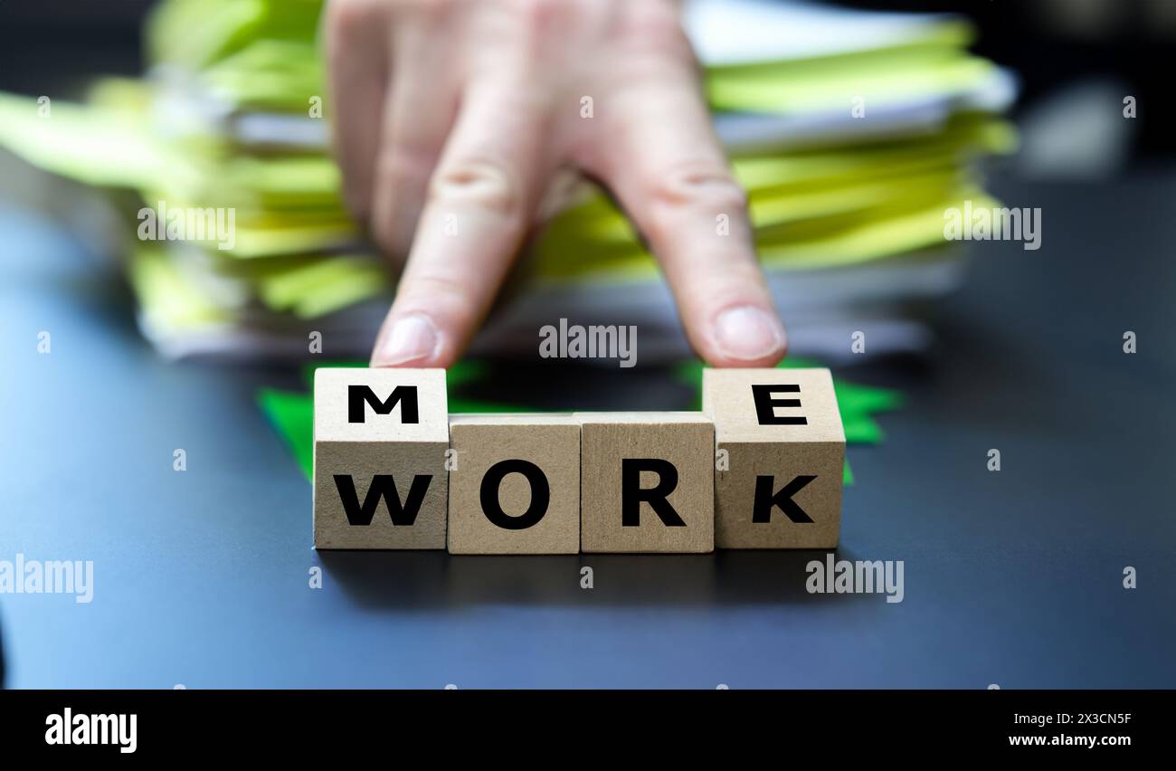 Würfel auf einem Schreibtisch bilden den Ausdruck „mehr Arbeit“. Stockfoto