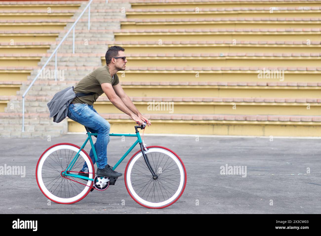 Ein fokussierter Mann in lässiger Kleidung fährt in einer urbanen Umgebung ein Fahrrad mit festem Gang, mit einer Kuriertasche über der Schulter, die den aktiven, umweltfreundlichen tran darstellt Stockfoto
