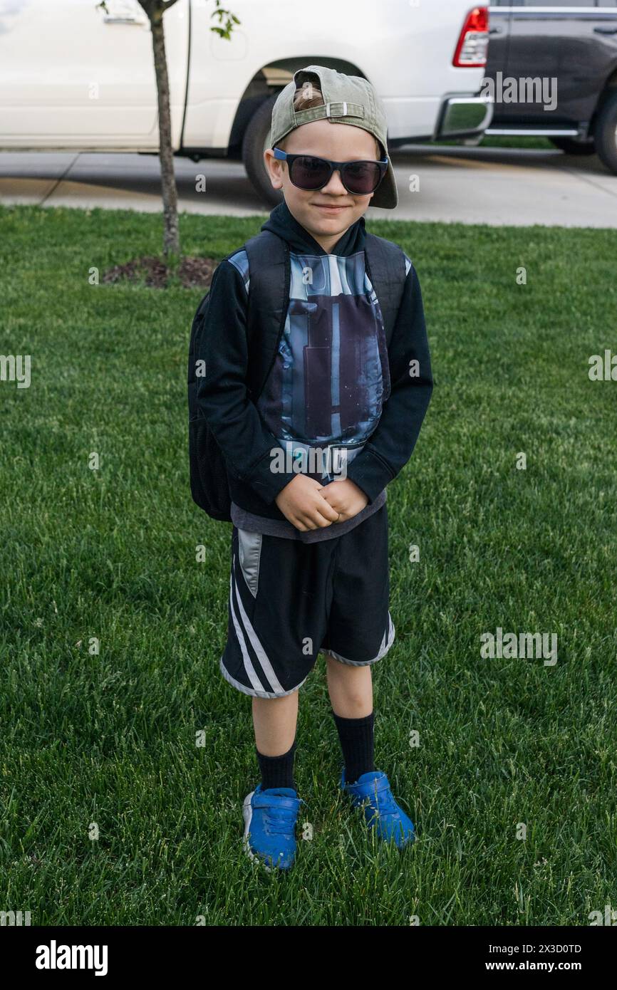 Lächelnder Junge in Mütze und Sonnenbrille, bereit für das Schulabenteuer Stockfoto