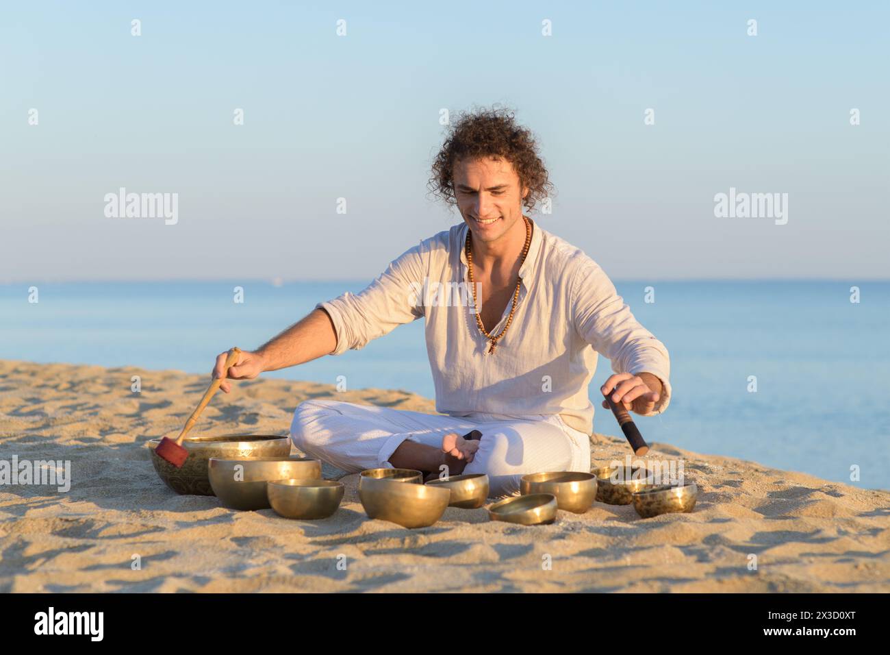 Lächelnder Mann, der auf dem Meer sitzt und auf tibetischen Klangschalen spielt Stockfoto