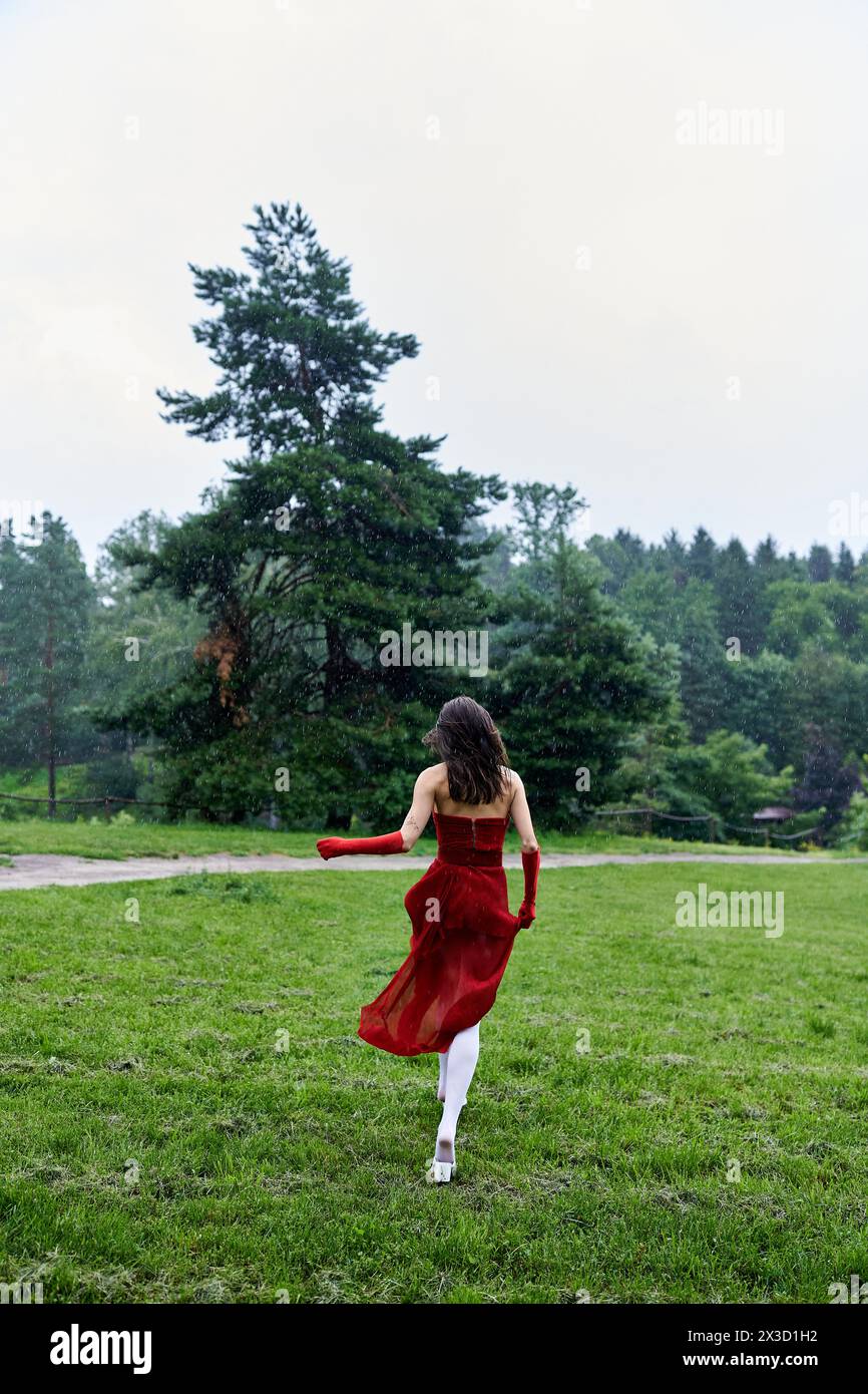 Eine junge Frau in einem fließenden roten Kleid und langen Handschuhen, die fröhlich durch ein üppiges Feld läuft und Freiheit und Bewegung verkörpert. Stockfoto