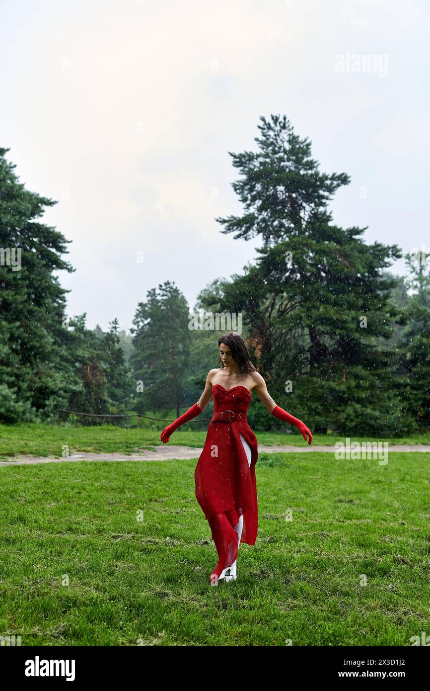 Eine junge Frau in einem karmesinroten Kleid und langen Handschuhen steht anmutig in einem pulsierenden Feld und umhüllt die Sommerbrise. Stockfoto