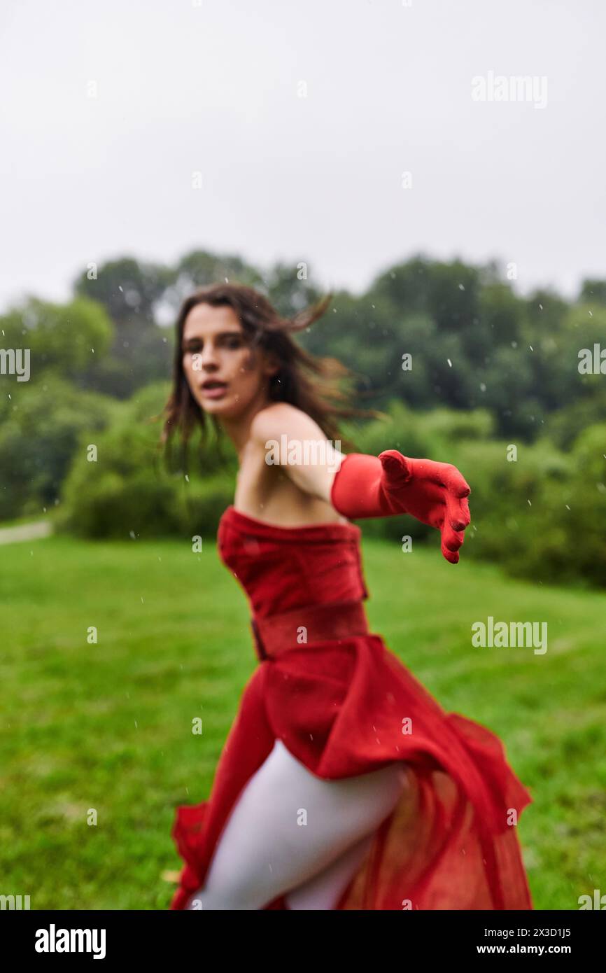 Eine anmutige junge Frau in einem leuchtend roten Kleid und langen Handschuhen wirbelt fröhlich inmitten der natürlichen Schönheit eines sonnendurchfluteten Feldes. Stockfoto