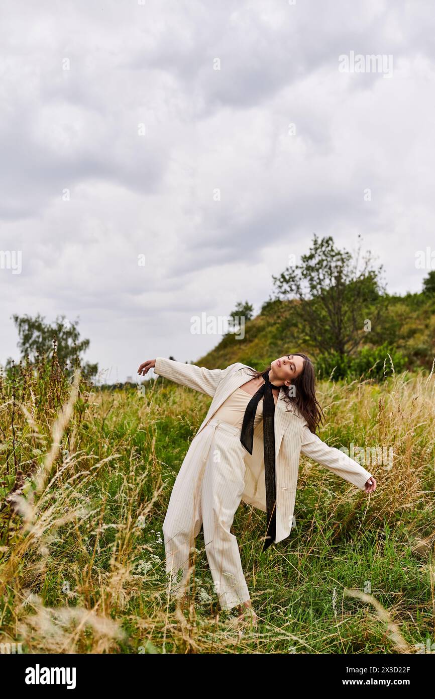 Eine junge Frau steht auf einem Feld, die Arme gestreckt, in weißer Kleidung, die Sommerbrise spürt und die Schönheit der Natur umhüllt. Stockfoto