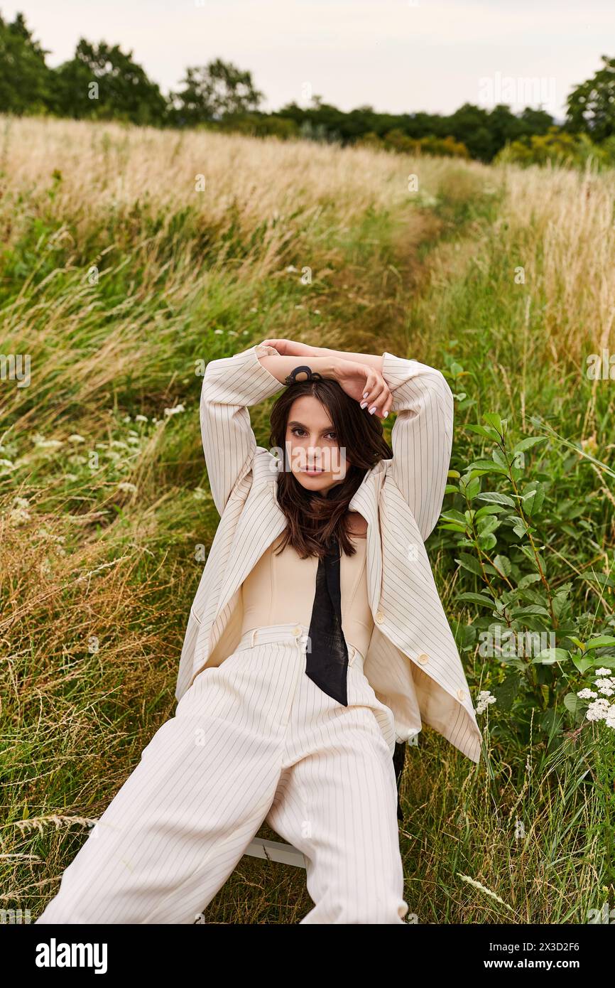 Eine schöne junge Frau in weißer Kleidung, die auf einem Feld sitzt, mit den Händen auf dem Kopf, die Sommerbrise liebend. Stockfoto