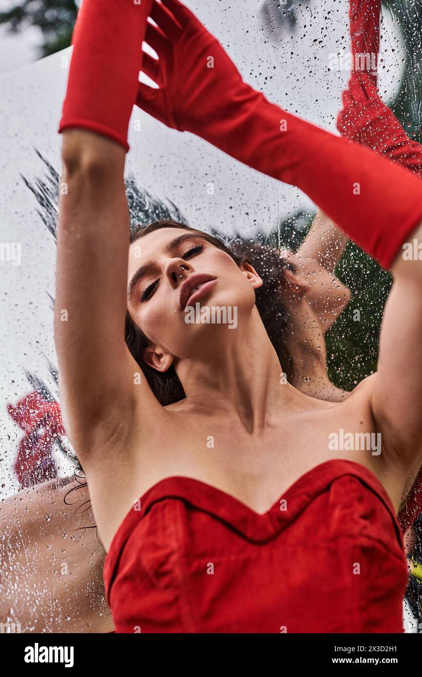 Eine anmutige junge Frau in einem leuchtend roten Kleid und langen Handschuhen steht friedlich und umhüllt die Sommerbrise in der Natur. Stockfoto