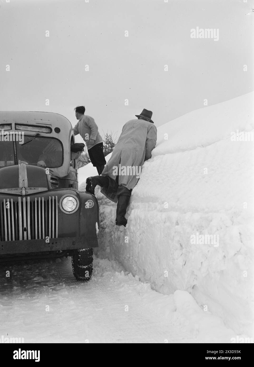 Aktuell 05–1951: Südnorwegen mit Schnee bedeckt. Vier bis fünf Meter hohe Pflugkanten entlang der Straßen, der Schnee ist so hoch, dass man leicht aus dem zweiten Stock gehen kann und die Leute ständig auf die Dächer klettern müssen, um den Schnee von dort weg zu räumen. Fußgänger, die den Bus vor den Treffpunkten treffen, haben nichts zu tun, als mühsam an den Pflugrändern vorbei zu klettern, um sich selbst zu retten.Foto: Arne Kjus / aktuell / NTB ***Foto ist nicht bildbearbeitet*** dieser Bildtext wird automatisch übersetzt Stockfoto