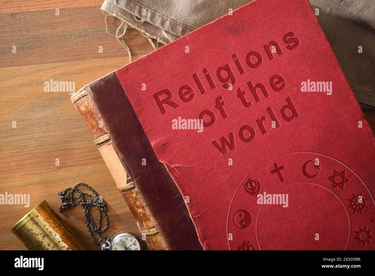 Detail des alten Buches über das Studium der Religionen in der Welt mit graviertem Text und Symbolen verschiedener Religionen auf Holztisch mit dekorativen Objekten. Stockfoto