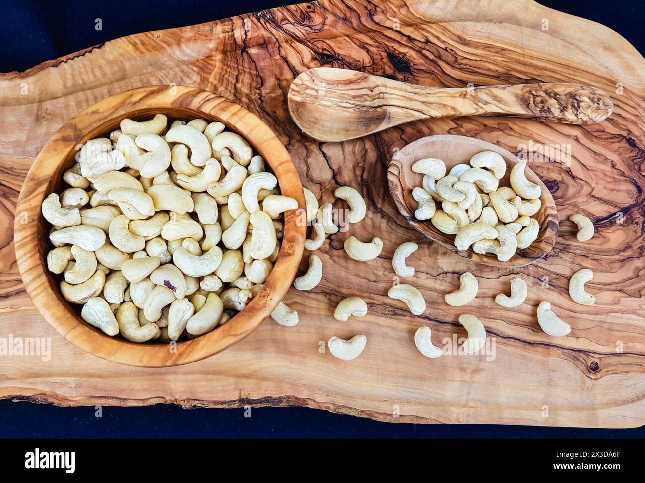Cashewnüsse (Anacardium occidentale), Cashewnüsse in Holzschalen mit einem Holzlöffel auf einem Brett Stockfoto