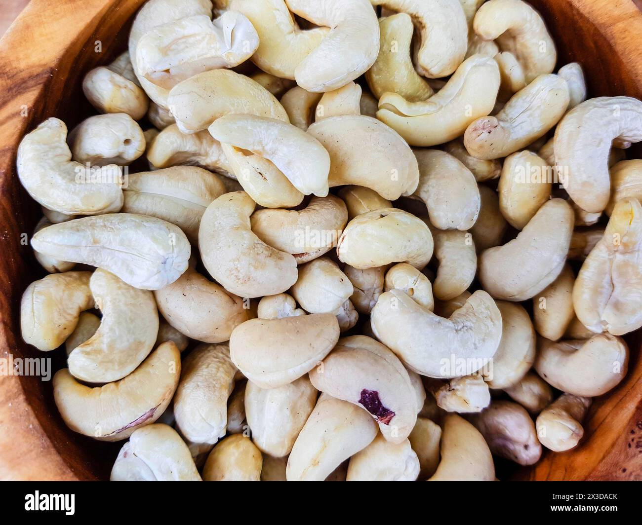 Cashewnüsse (Anacardium occidentale), Cashewnüsse in einer Holzschale auf einem Holztisch Stockfoto