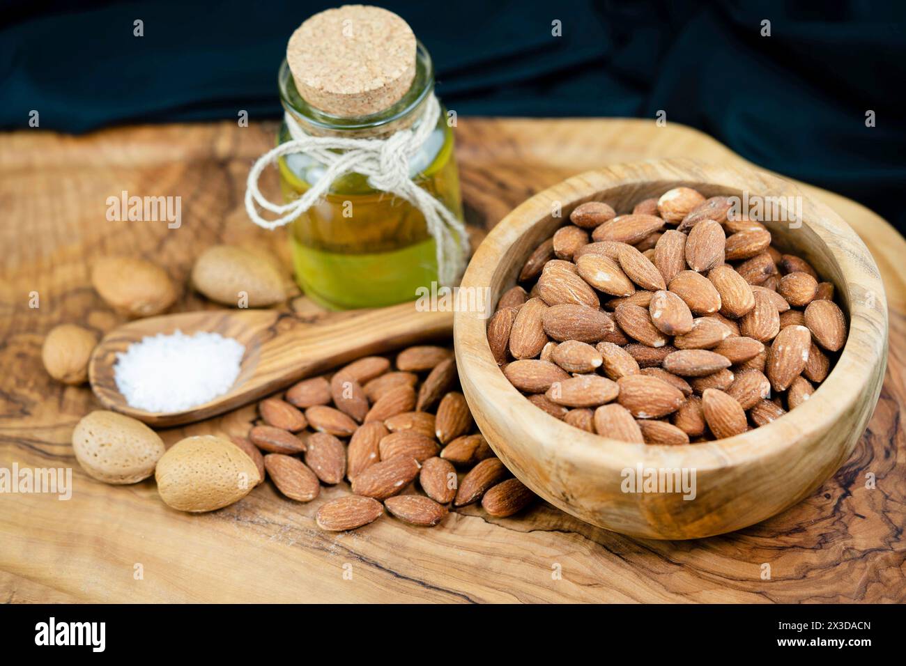 Mandel (Prunus dulcis, Prunus amygdalus, Amygdalus communis, Amygdalus dulcis), gesalzene Mandeln in einer Holzschale mit ungesackten Mandeln, Löffel mit sal Stockfoto