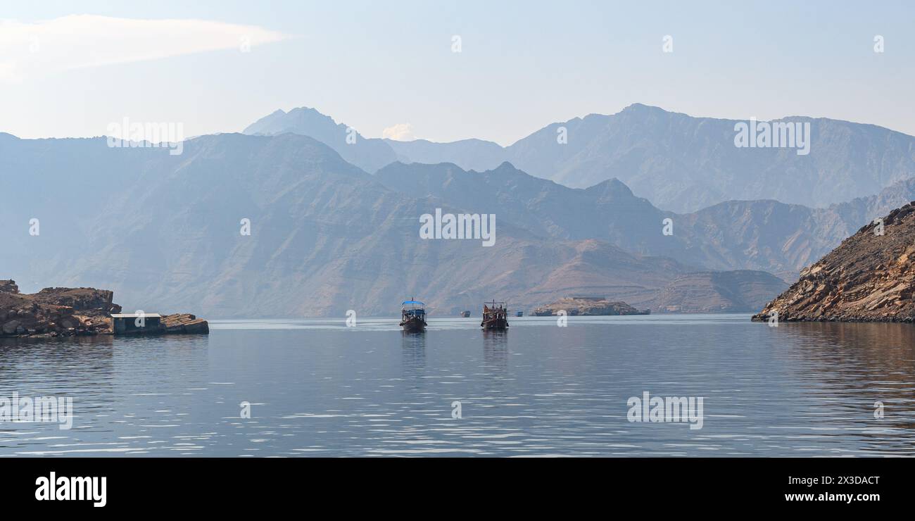 Zwei Boote segeln sanft durch das ruhige Wasser der Fjorde von Khasab, umgeben von der majestätischen Umarmung zerklüfteter Berge, und enthüllen eine Reise, wo Sie hinkommen Stockfoto