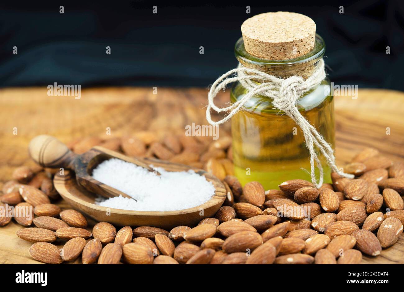 Mandel (Prunus dulcis, Prunus amygdalus, Amygdalus communis, Amygdalus dulcis), gesalzene Mandeln, Holzlöffel mit Salz und einer Flasche Mandelöl Stockfoto